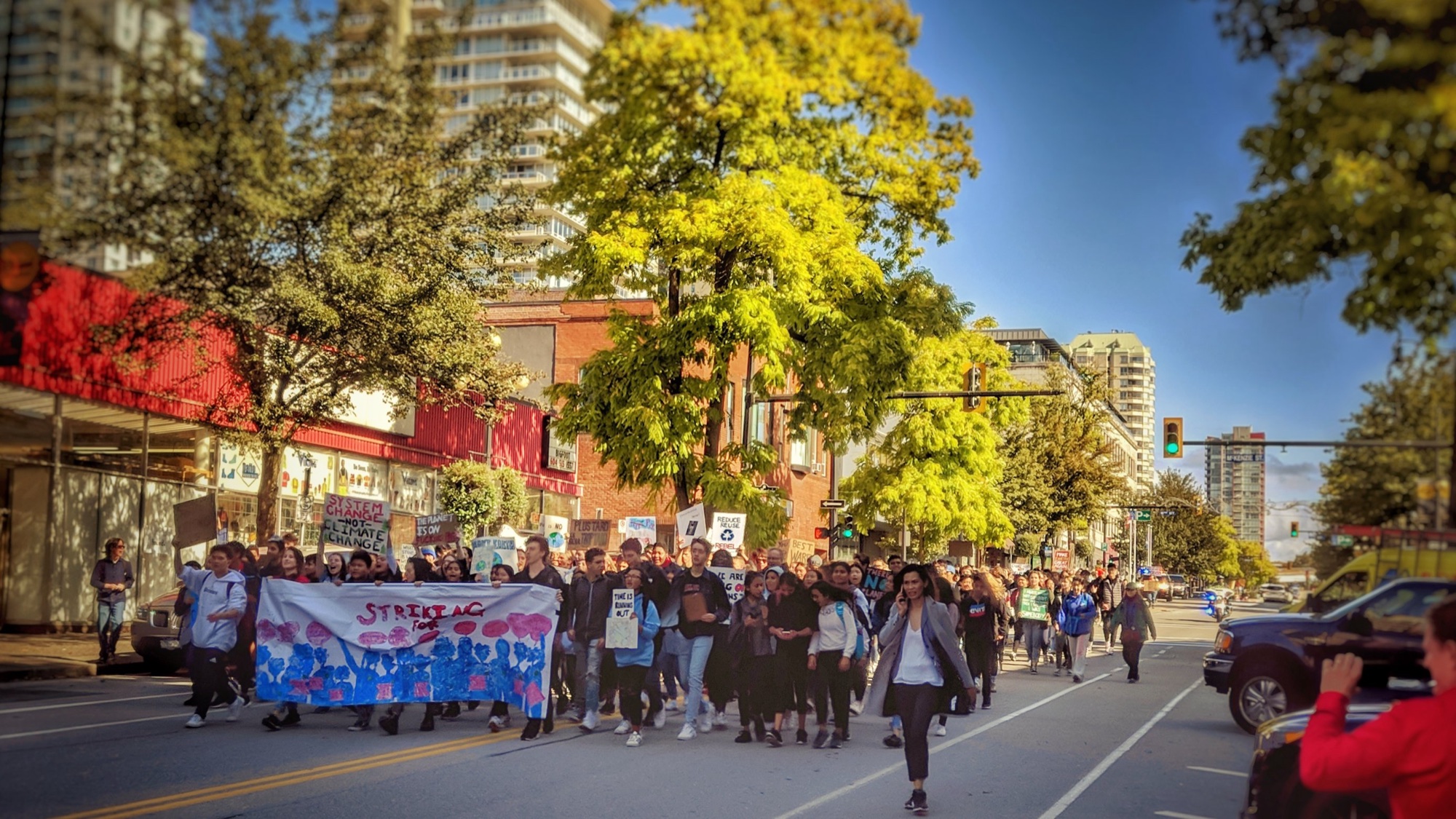 A large group of young climate strikers marching down a city street with handmade signs