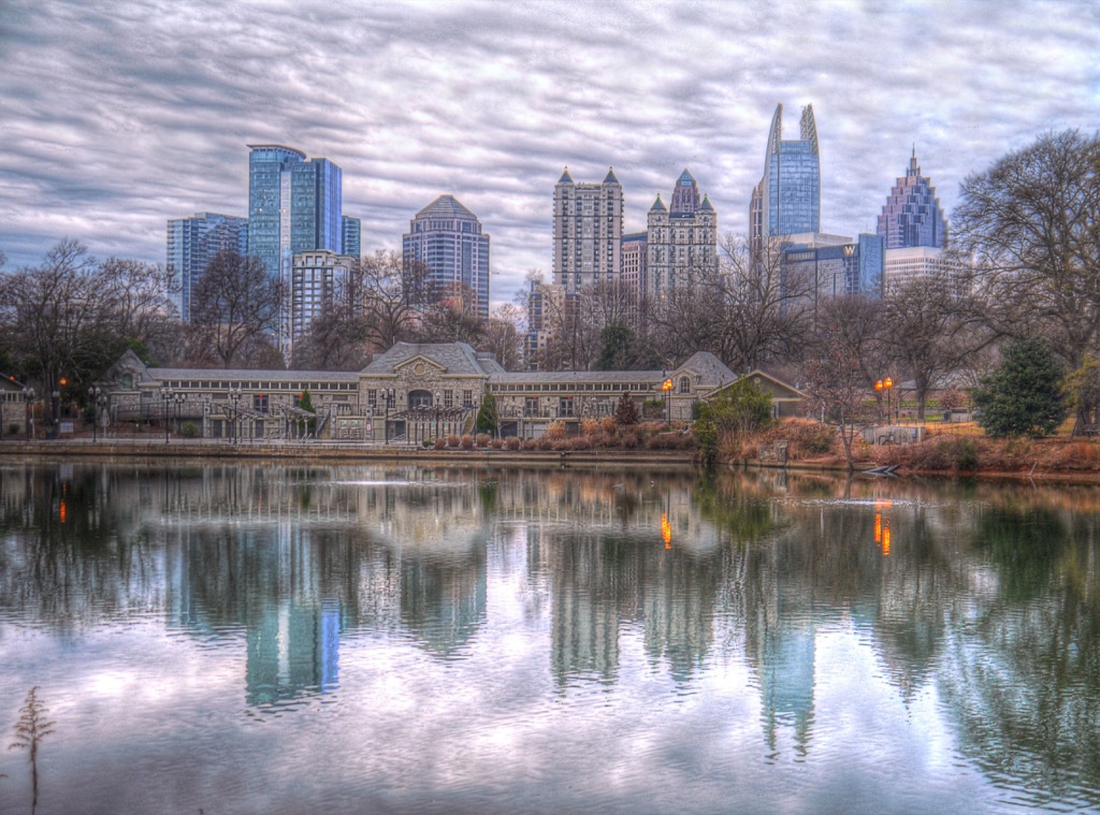 A city skyline reflected in a lake behind an urban park